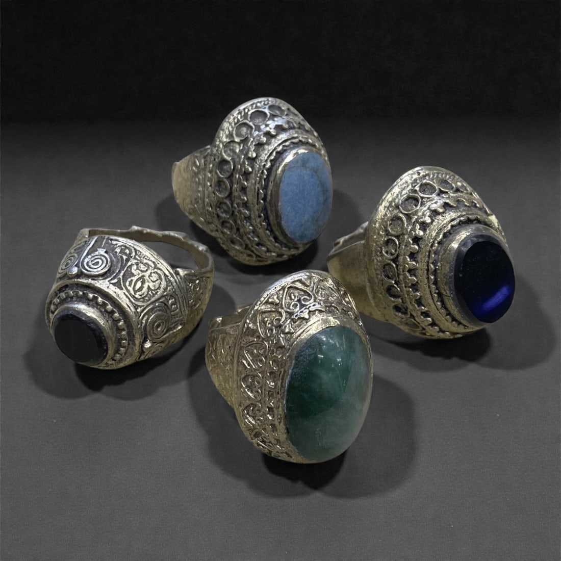 A Group of Four Antique Silvered Bronze Rings, 19th Century, Size 7.5-8US, 62g, 64AA: Each ring is crafted from silvered bronze, featuring ornate metalwork including filigree, repousse, and granulation details. The bezels are set with composite stones, the surfaces exhibit minor patina