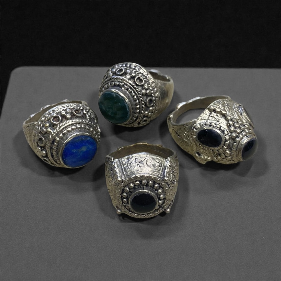 A Group of Four Antique Silvered Bronze Rings, 19th Century, Size 8-8.5US, 58g, 60AA: Each ring is crafted from silvered bronze, featuring ornate metalwork including filigree, repousse, and granulation details. The bezels are set with composite stones, the surfaces exhibit minor patina