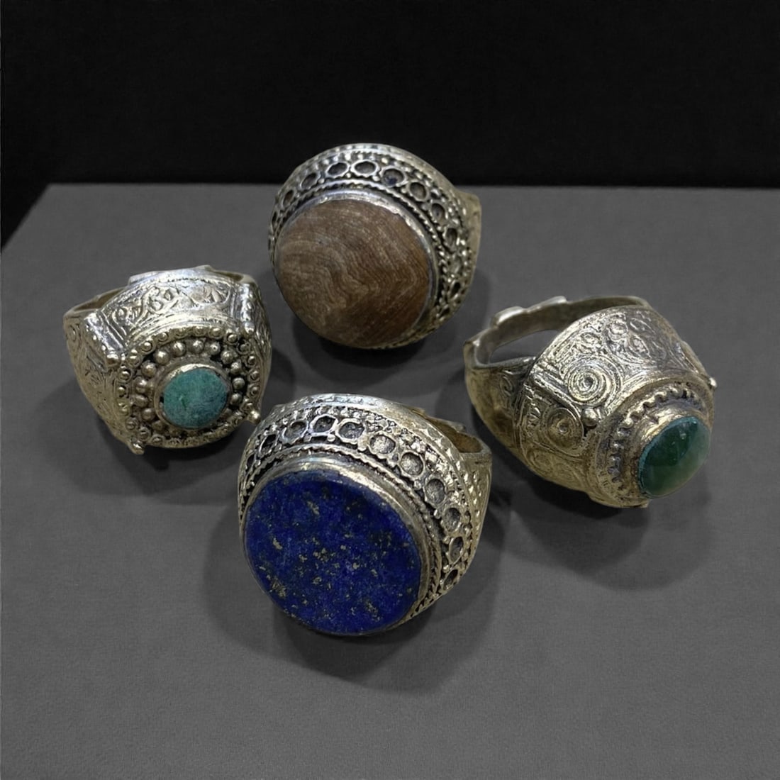 A Group of Four Antique Silvered Bronze Rings, 19th Century, Size 8US, 54g, 63AA: Each ring is crafted from silvered bronze, featuring ornate metalwork including filigree, repousse, and granulation details. The bezels are set with composite stones, the surfaces exhibit minor patina
