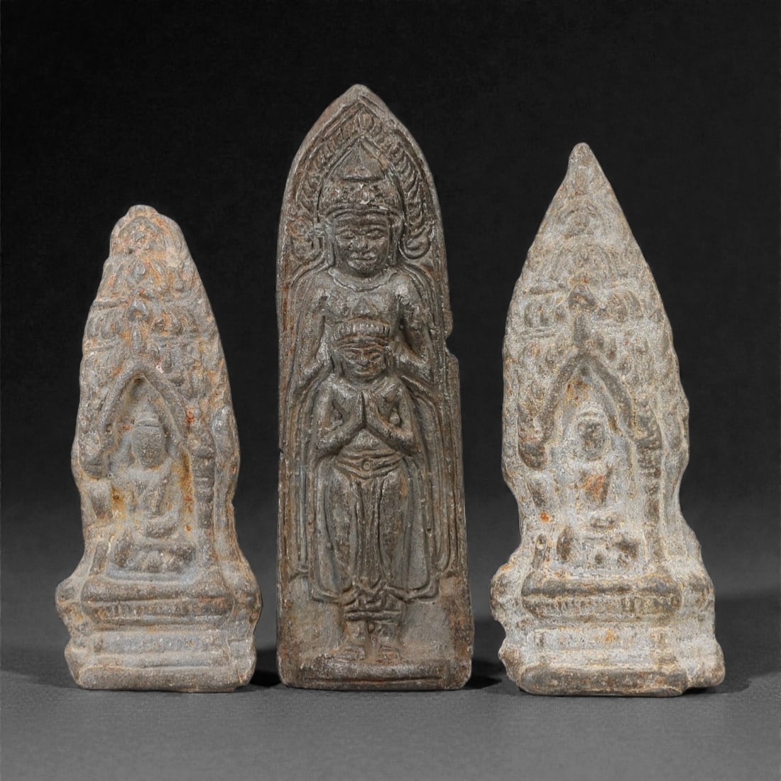 A Group of Three Thai Metal Buddhist Amulet Plaques, 20th Century, 43FL: Each amulet is formed from a dark metal alloy with natural surface patination, corrosion, and minor wear consistent with age and use. The left and right plaques depict a seated Buddha within an arched