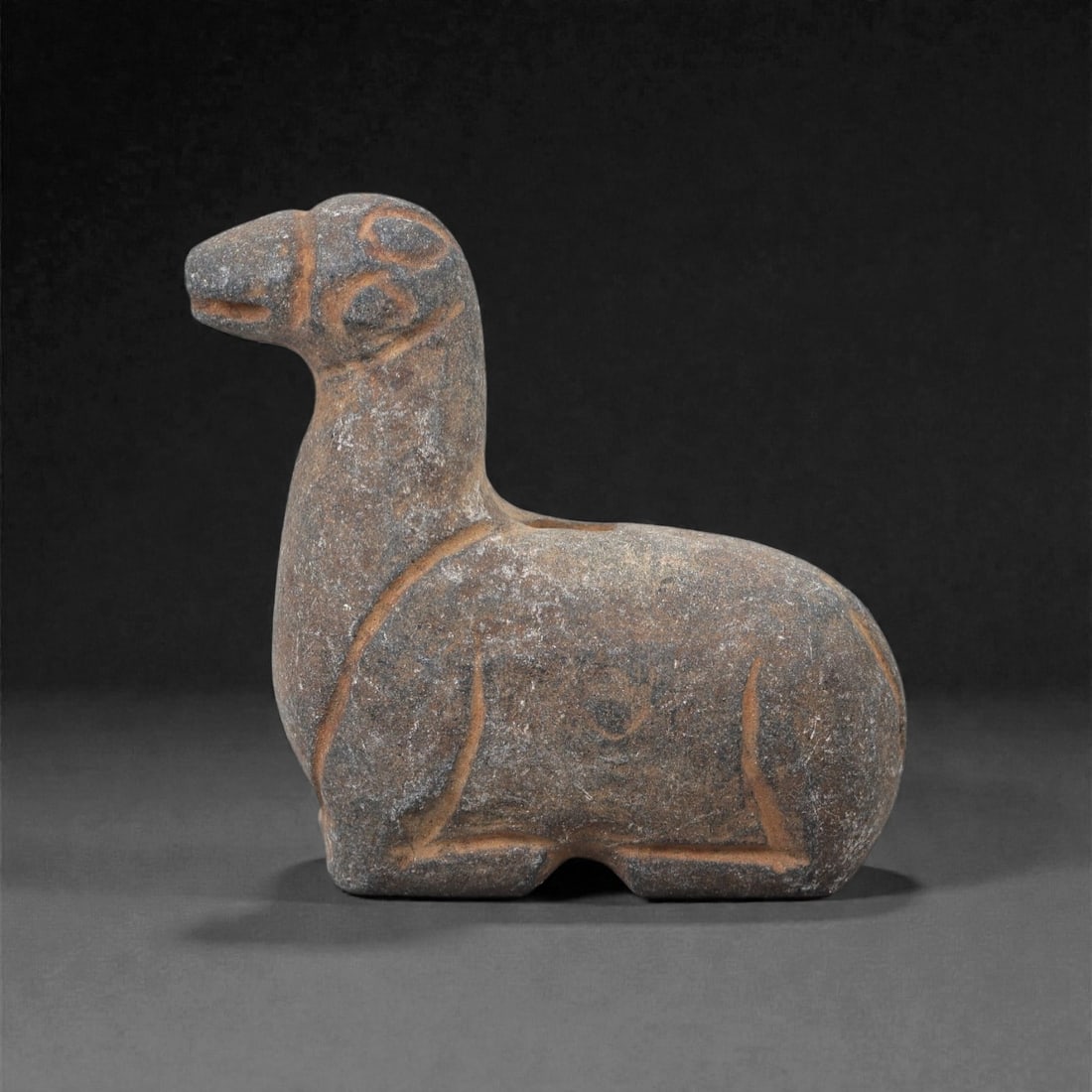 An Ancient Near Eastern Stone Zoomorphic Amulet, 3rd-1st Millennium BCE, 69FL: Carved from greyish-brown stone with a granular, weathered surface and orange-brown incised lines, the amulet depicts a stylized quadrupedal animal, likely a camel or similar beast, in a standing pose