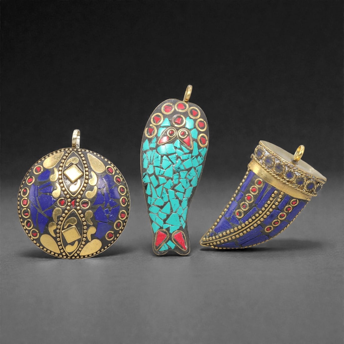 A Group of Three Tibetan Inlaid Metal Pendants, 20th Century, 92ZG: Comprising three pendants, each constructed from a metal base with inlaid semi-precious stones and gold-toned metalwork. The first pendant is circular, with a silver-toned metal base inlaid with lapis