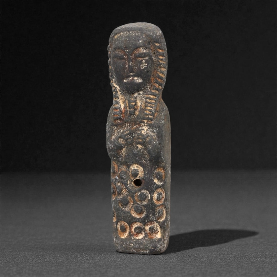 A Medieval Sino-Siberian Steatite Idol, 10th-14th Century CE, 65FL: Carved from dark grey steatite with scattered light grey and orange-brown surface encrustation, the idol depicts a standing human figure in a stylized form. The head is rounded with closed eyes, a pro