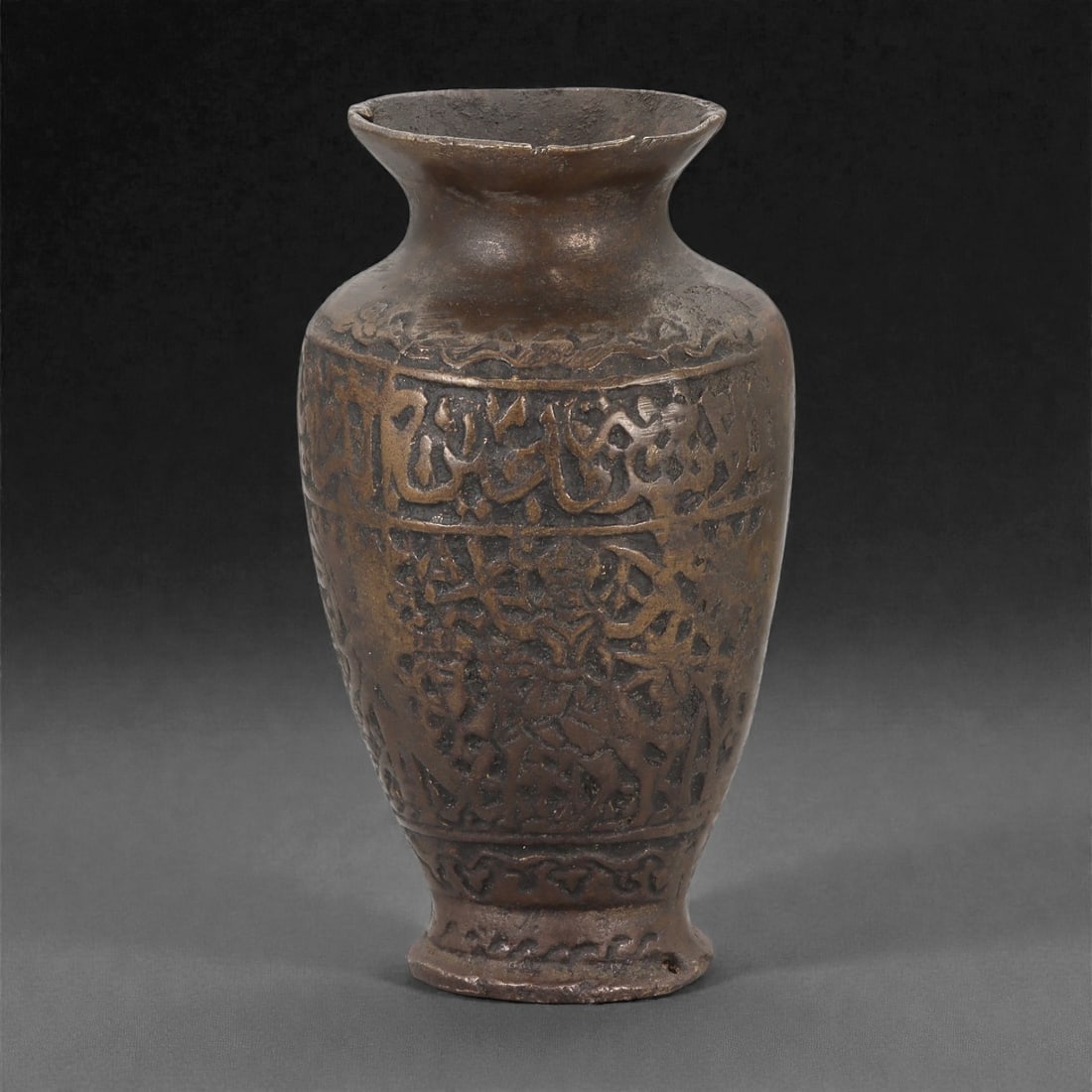 An Indo-Islamic Bronze Vase with Arabic Inscription, 12th-14th Century CE, 9LM: Cast in bronze with a dark brown patina, the vase has a rounded body rising to a gently flaring neck and outward-turned rim. The exterior is decorated in low relief with bands of Arabic calligraphy en