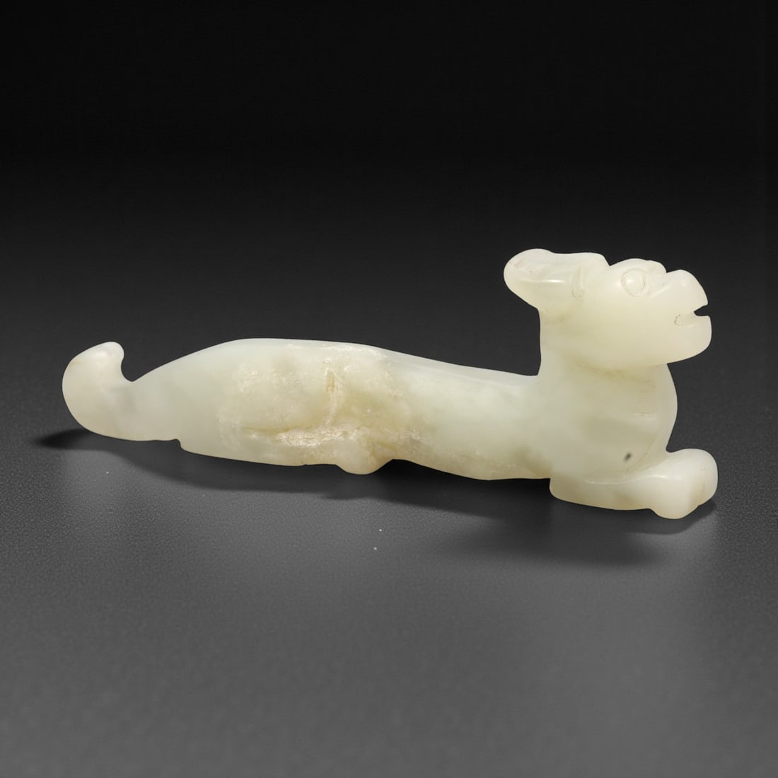 A Chinese Hetian Jade Zoomorphic Figure, 20th Century, 54FH: Carved from pale creamy-white Hetian jade with areas of cloudy translucency and minor natural inclusions, the figure is worked in the round and modeled as a recumbent animal with an elongated body. Th