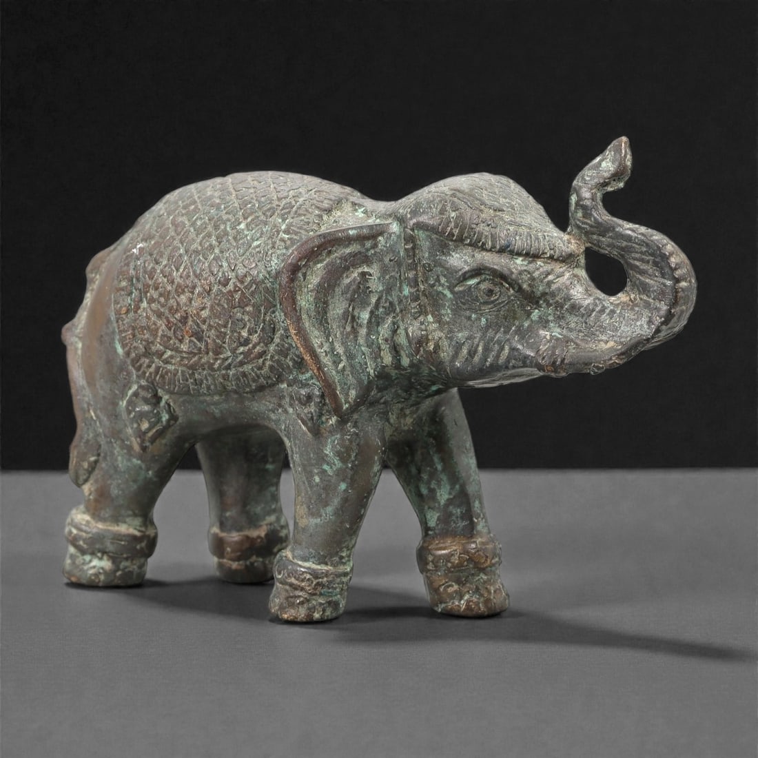 A Southeast Asian Bronze Elephant Figure, 20th Century, 20FJ: Cast in bronze, the figure represents a standing elephant shown in profile with the trunk raised and gently curved. The body is modeled with simplified but clearly articulated anatomical features, inc