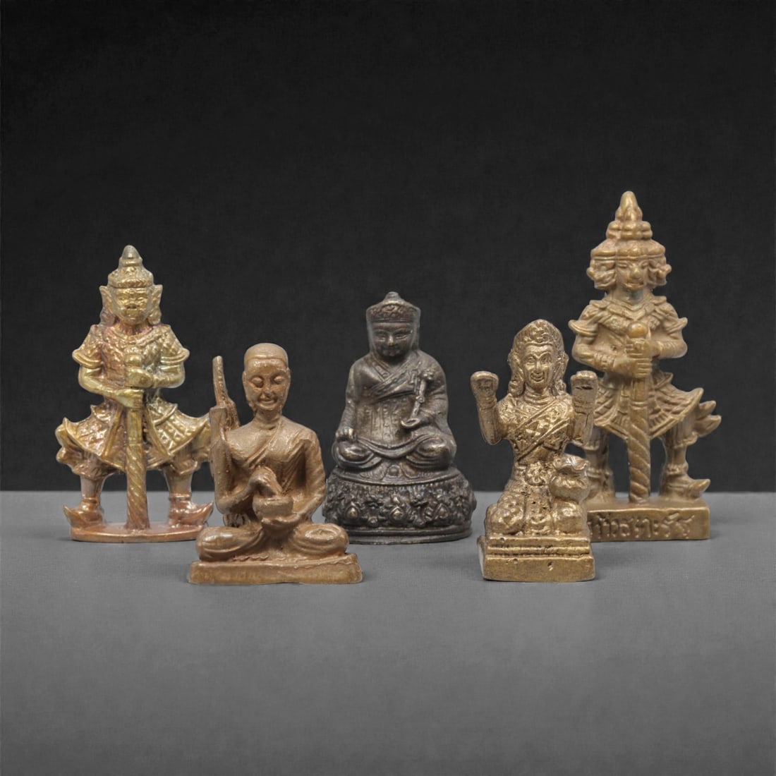 Five Thai Bronze Buddhist and Guardian Miniature Figures, 20th Century, 18FM: Cast from bronze with varied patination, the set comprises five miniature devotional figures: two guardian figures with ornate headdresses and armor, two seated Buddhist monks, and a seated deity with