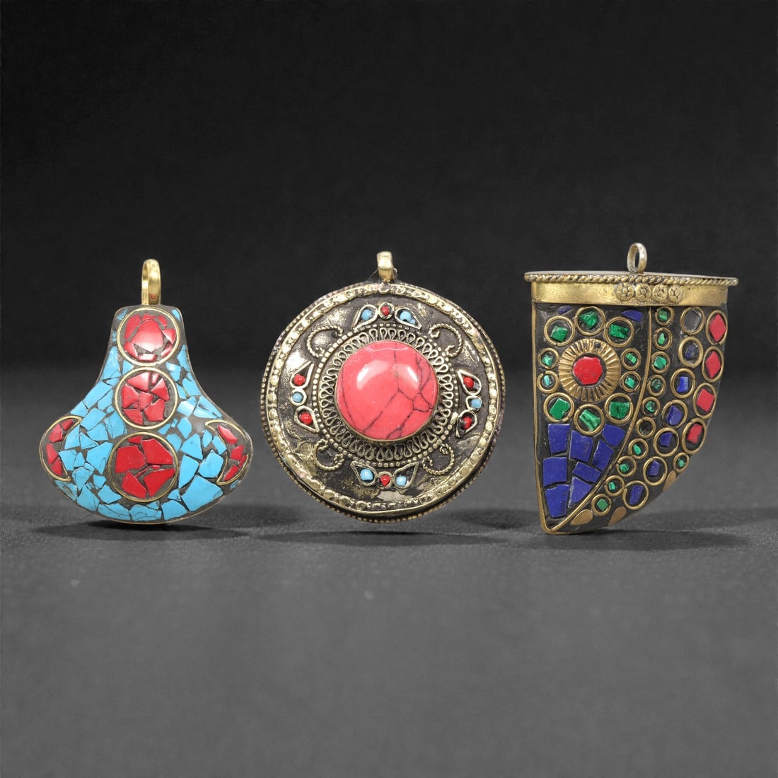 A Group of Three Tibetan Inlaid Metal Pendants, 20th Century, 89ZG: Comprising three pendants, each constructed from a metal base with inlaid semi-precious stones and decorative metalwork. The first pendant is gourd-shaped, with a dark metal base inlaid with turquoise