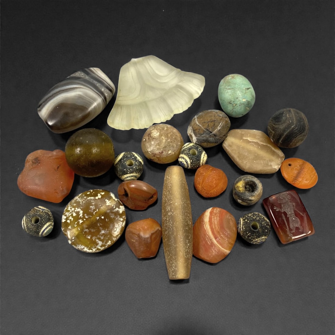A Mixed Group of Carnelian, Agate, and Glass Beads, Ancient and Antique Periods, 34V: Comprising twenty-two beads of varied forms and materials, the group includes elements carved or formed from carnelian, agate, glass, and related siliceous materials, ranging from spherical and flatte
