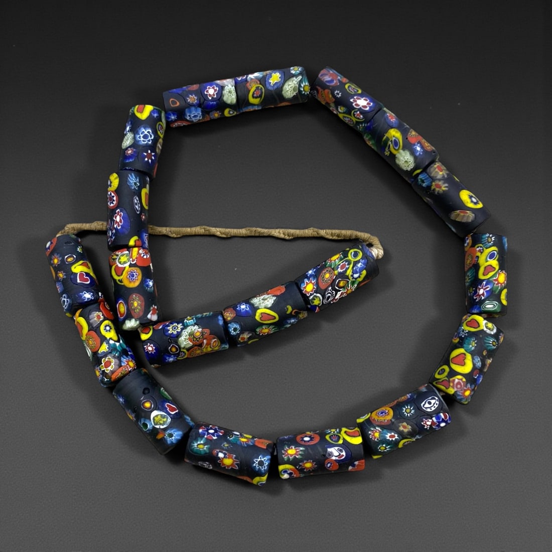 A Venetian Glass Millefiori Cylindrical Bead Necklace Strand, 19th Century, 217g, 8AA: Composed of cylindrical glass beads decorated with millefiori canes, featuring a deep black ground densely inlaid with colorful floral and geometric motifs in red, yellow, blue, and white, strung on a
