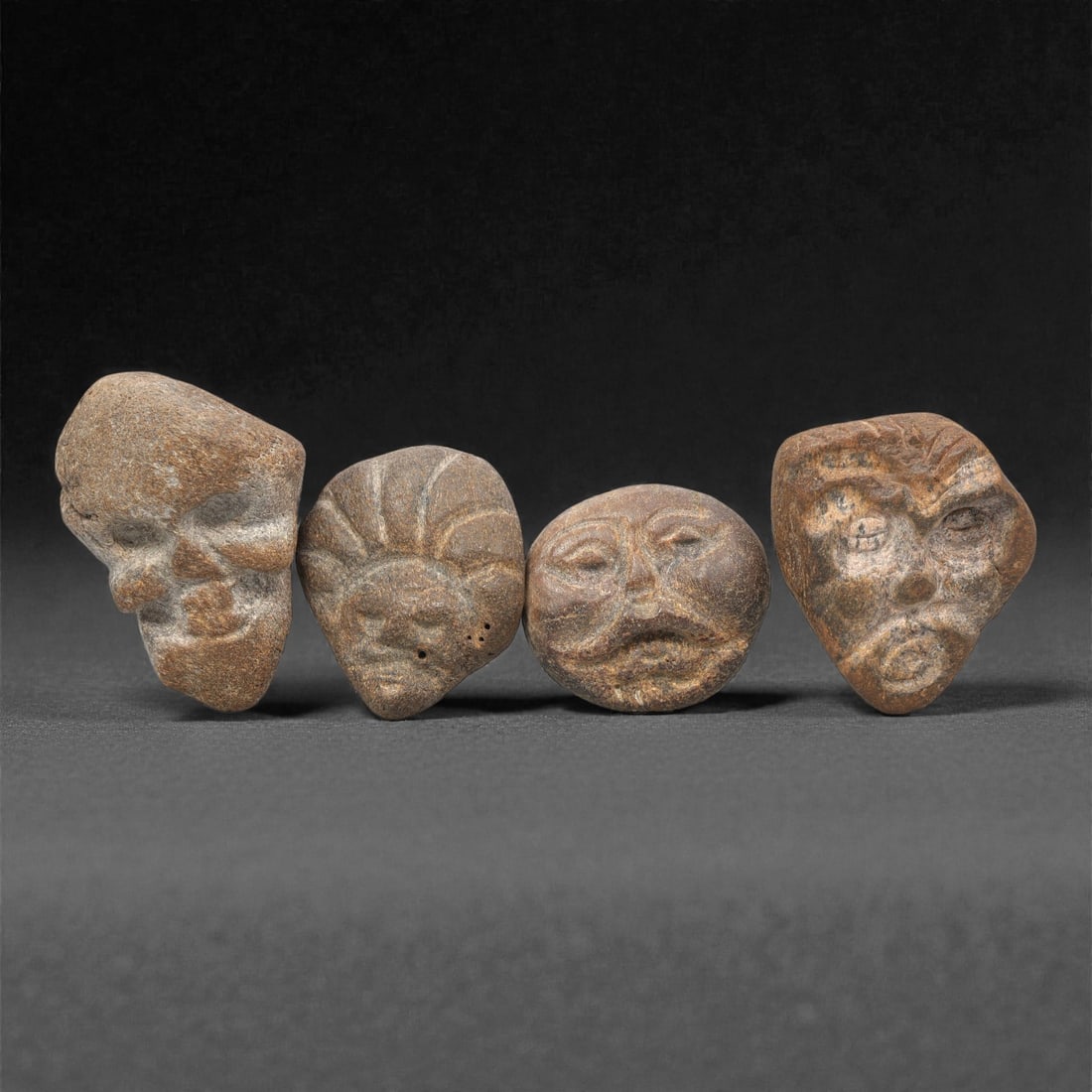A Group of Four Ancient Bone Maskettes, 2nd-1st Millennium BCE, 98ZG: Comprising four distinct bone maskettes, each carved from weathered bone with natural tonal variation and surface patination. The first, of light brown bone, is irregularly shaped with recessed facial