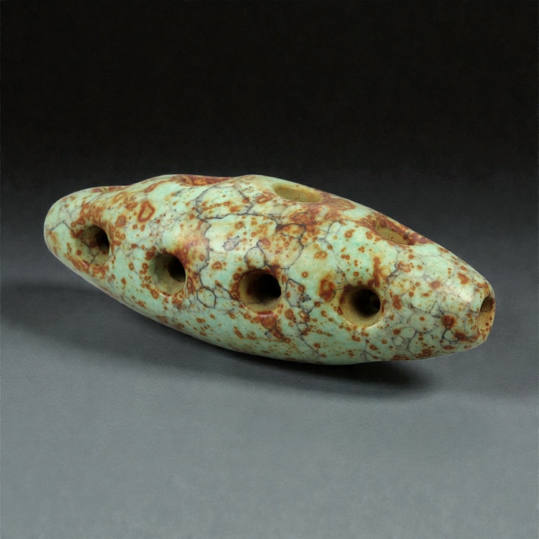 A Tibetan Turquoise Bead, 19th-20th Century, 99FC: Carved from pale green turquoise with extensive natural matrix and iron-rich veining, the bead is formed as an elongated, slightly flattened ovoid. The surface displays a mottled pattern of brown and