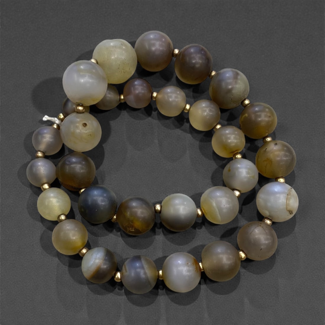 A West African Glass Mosaic Bead Necklace Strand, 19th-Early 20th Century, 136g, 15AA: Composed of spherical glass beads with a dark blue ground decorated with swirling, irregular patterns of yellow, red, and green, strung on a modern braided fiber cord. The multi-colored mosaic effect