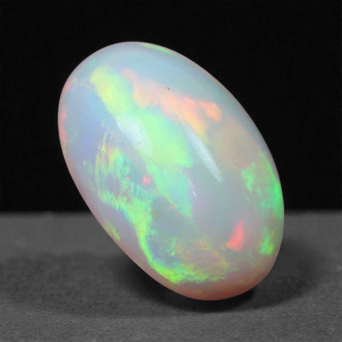 4.68 Carats Neon Grove Welo Opal - Natural Ethiopian Gemstone 14.9x9.8x6.6mm, 36XH: This electrifying Welo opal pulses with radiant greens, vivid oranges, and flashes of cherry red, set against a softly translucent body that glows like mist-lit foliage. The gemstone's internal fire p