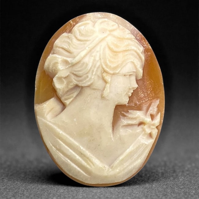 A European Shell Cameo, 20th Century, 100FH: Carved from layered shell with a pale white upper stratum set against a light brown ground, the cameo is oval in form and carved in relief with a right-facing female bust. The subject is rendered in a