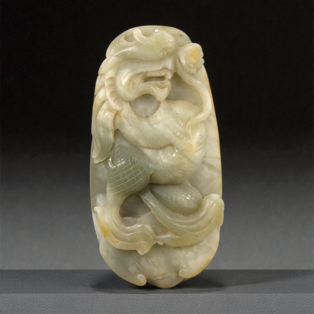 A Chinese Jade Dragon Plaque, 20th Century, 30FB: Carved from pale celadon jade with areas of milky translucency and faint yellow-brown inclusions, the plaque is worked in high relief with a sinuous dragon shown in a compact, coiled posture. The crea