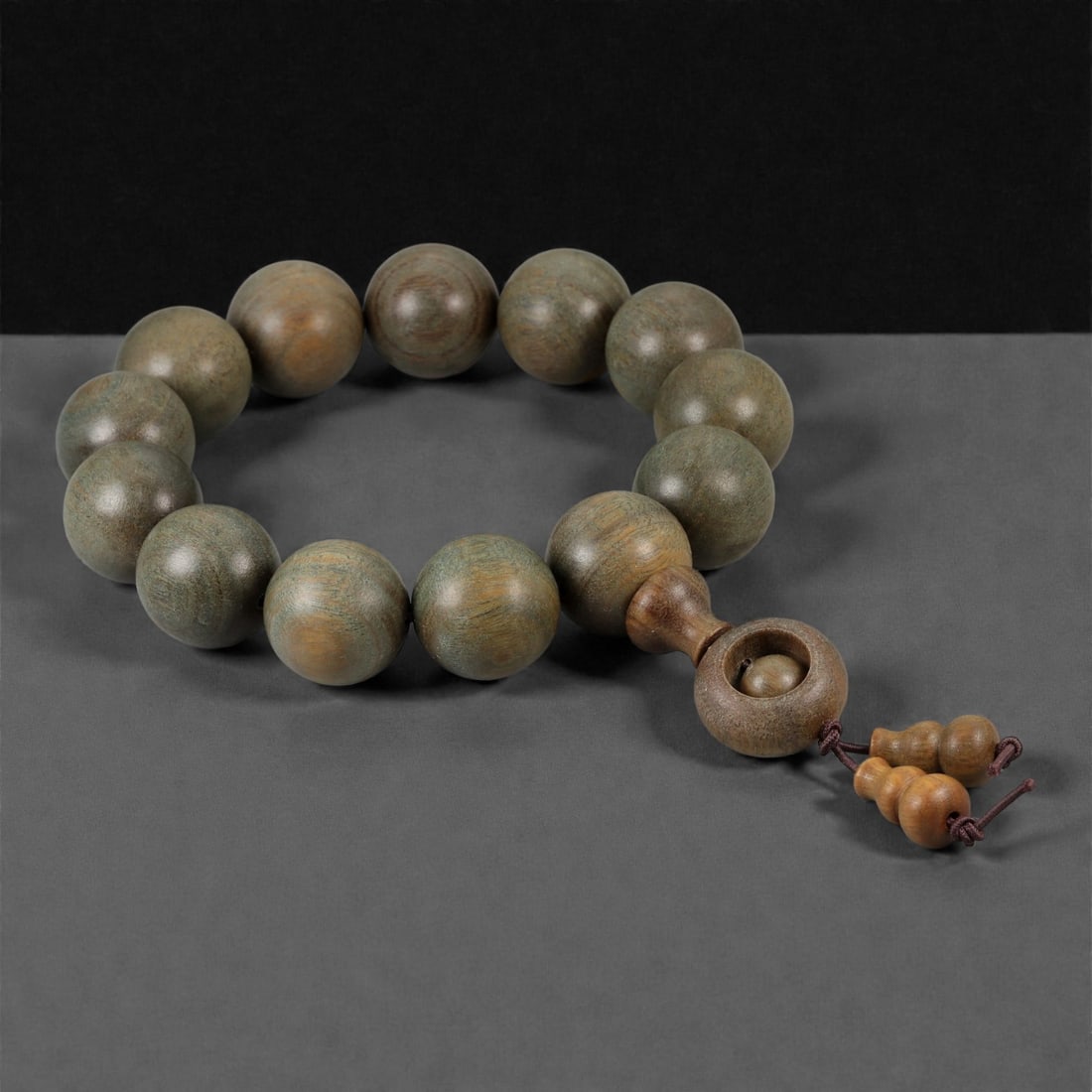 A Chinese Wood Bead Bracelet, 20th Century, 61FD: Composed of large spherical beads carved from wood with muted olive-brown to greenish-brown tonal variation, each bead smoothly polished to emphasize the natural grain and subtle surface mottling. The