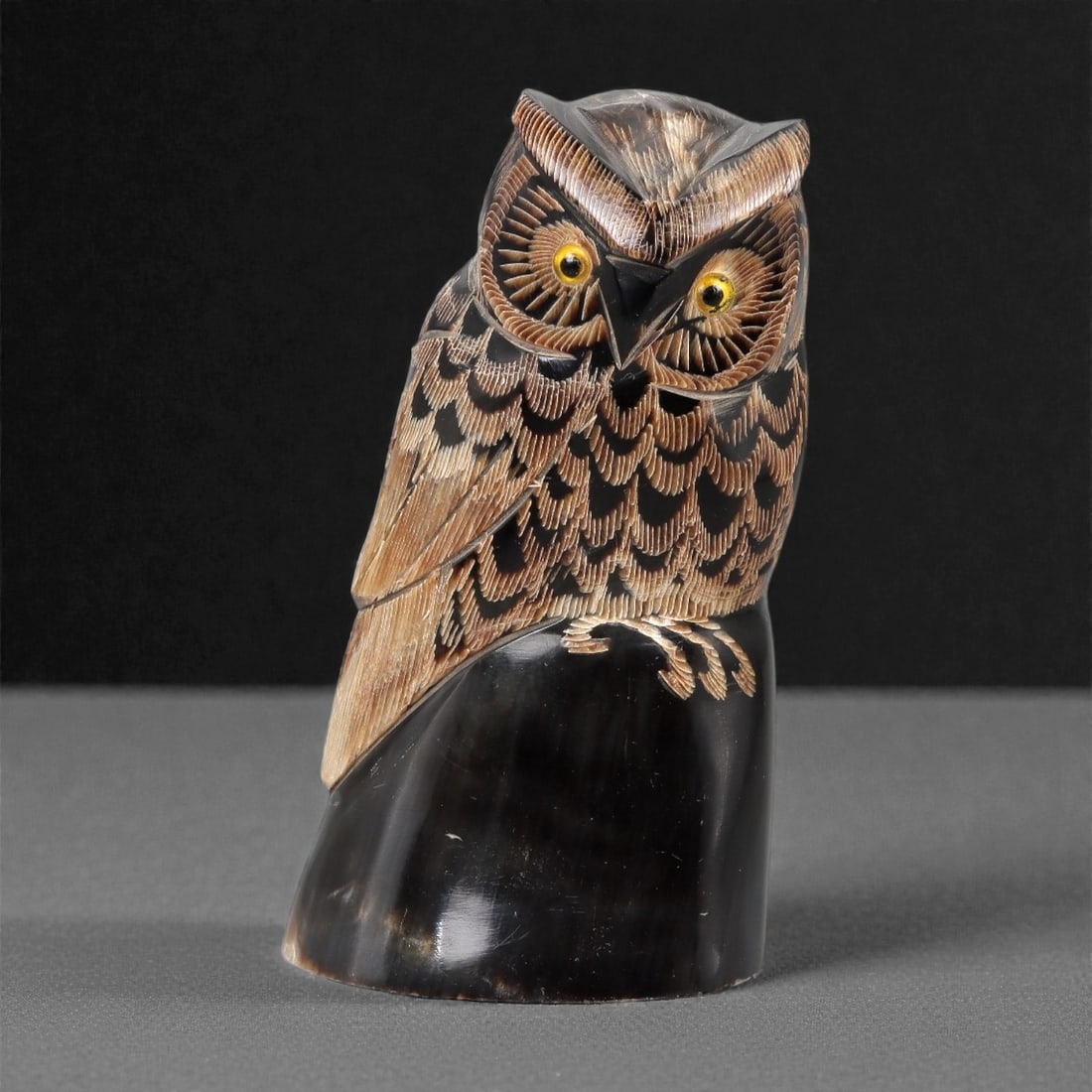 An East Asian Ox Horn Owl Effigy, 20th Century, 10FJ: Carved from a single section of dark ox horn with natural tonal variation and a polished surface, the object is formed as a standing owl rendered in the round. The head is modeled with prominent circu