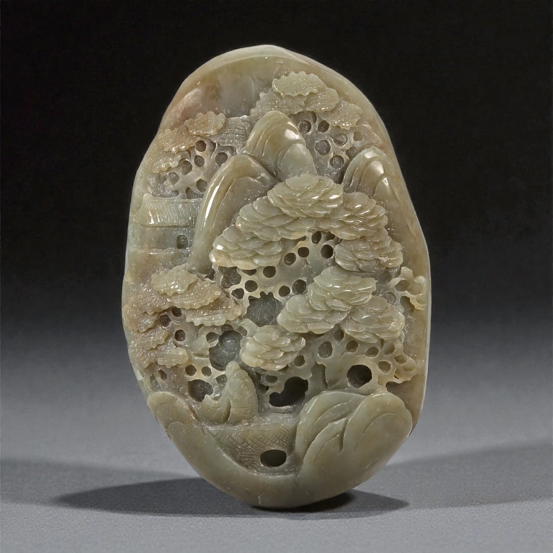 A Chinese Hetian Jade Pierced Landscape Display, 20th Century, 29FC: Carved from pale celadon Hetian jade with subtle gray and beige inclusions, the sculpture is worked as a freestanding display piece in the form of a miniature landscape. The composition features layer
