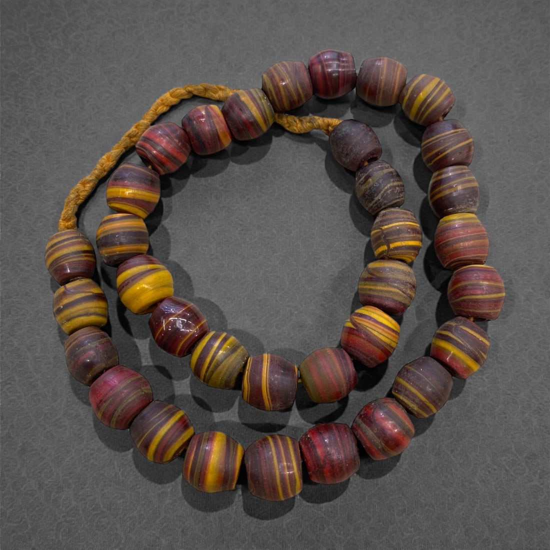 An Antique Venetian Glass Swirl Bead Necklace Strand, 19th Century, 185g, 31AA: Composed of rounded, disk-shaped glass beads with vibrant swirling patterns of deep red and golden yellow, strung on a period-style braided fiber cord. This bead style is characteristic of Venetian tr