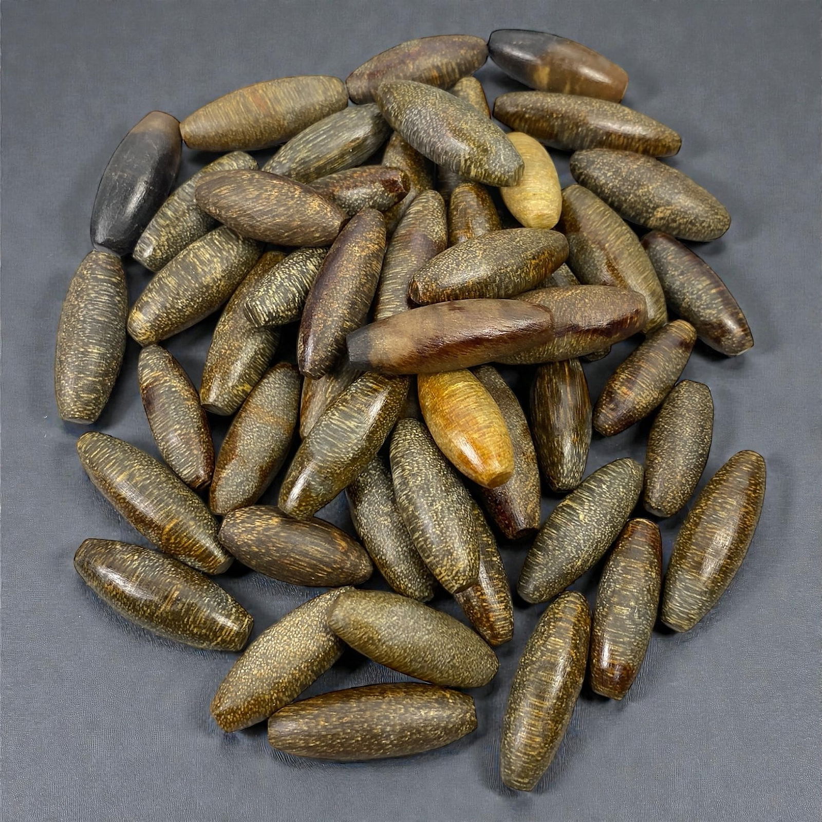 A Group of Himalayan Fossilized Wood Bead Blanks, 20th Century, 81V: Comprising a group of elongated bead-form elements fashioned from fossilized wood, exhibiting dark brown, olive, and ochre tones with fine linear grain patterns and dense mineralized texture. The bead