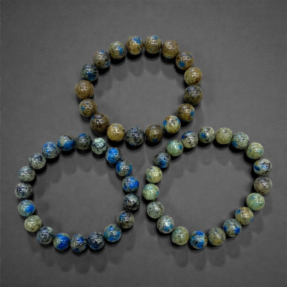 A Group of Three K2 Jasper Beaded Bracelets, 102g, 80AA: Comprising three stretch bracelets composed of polished spherical K2 Jasper beads. The beads display a distinctive mix of deep blue azurite inclusions set against a matrix of grey, beige, and green fe
