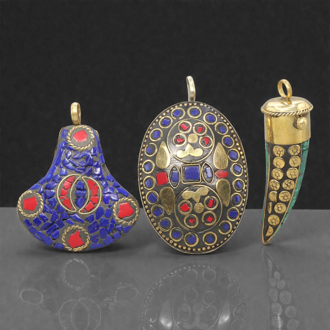 A Group of Three Tibetan Inlaid Metal Pendants, 20th Century, 90ZG: Comprising three pendants, each constructed from a metal base with inlaid semi-precious stones and gold-toned metalwork. The first pendant is gourd-shaped, with a dark metal base inlaid with lapis laz