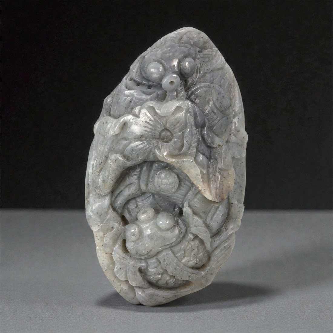 A Chinese Nephrite Jade Fish Carving, 20th Century, 19YB: Carved from pale grey nephrite jade with darker speckled inclusions and subtle tonal variation, the object is worked as a vertical composition featuring multiple fish arranged in a stacked and interlo