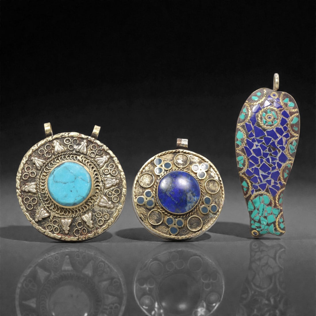 A Group of Three Tibetan Inlaid Metal Pendants, 20th Century, 86ZG: Comprising three pendants, each constructed from a metal base with inlaid semi-precious stones and decorative metalwork. The first pendant is circular, with a brass-toned metal base featuring a large