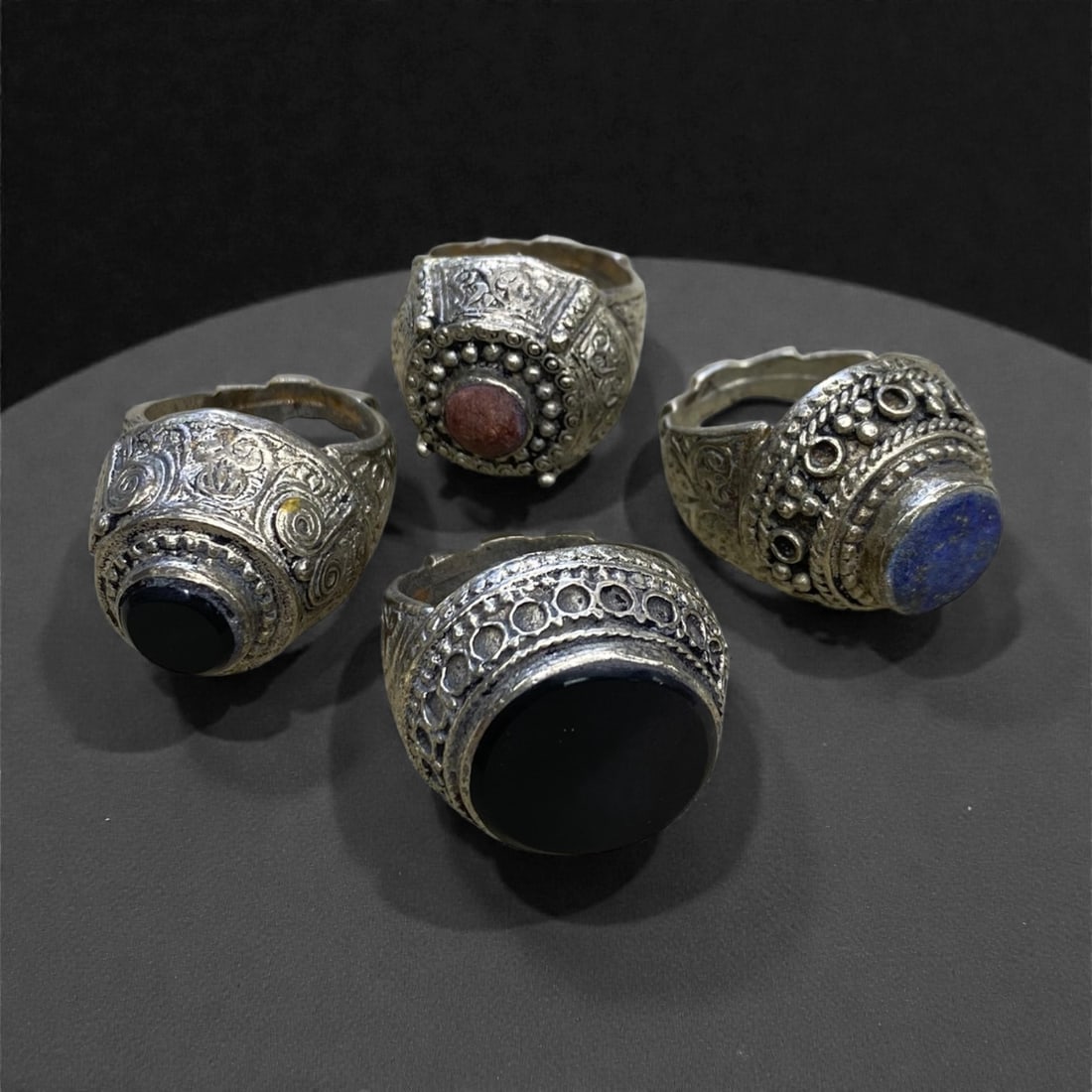 A Group of Four Antique Silvered Bronze Rings, 19th Century, Size 8-8.5US, 54g, 66AA: Each ring is crafted from silvered bronze, featuring ornate metalwork including filigree, repousse, and granulation details. The bezels are set with composite stones, the surfaces exhibit minor patina
