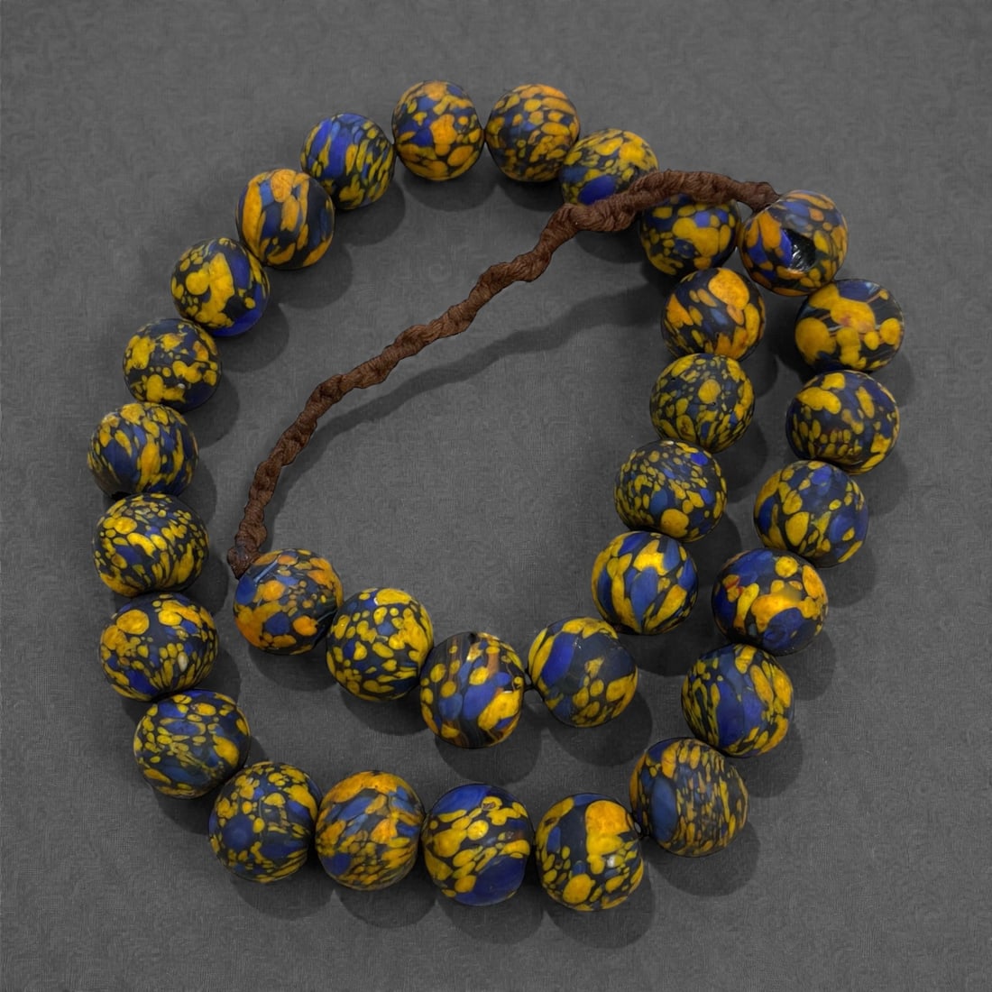 A West African Glass Mosaic Bead Necklace Strand, 19th-Early 20th Century, 262g, 13AA: Composed of spherical glass beads with a deep blue ground decorated with irregular yellow mottling, strung on a modern braided fiber cord. The mosaic pattern is characteristic of West African glass be