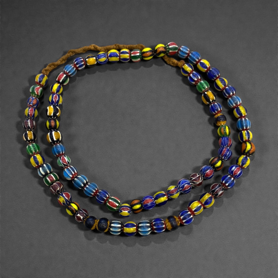 A Venetian Glass Chevron Bead Necklace Strand, 19th Century, 64g, 20AA: Composed of small, cylindrical glass beads decorated with concentric chevron patterns in alternating bands of blue, red, yellow, and green, strung on a modern braided fiber cord. The layered chevron d