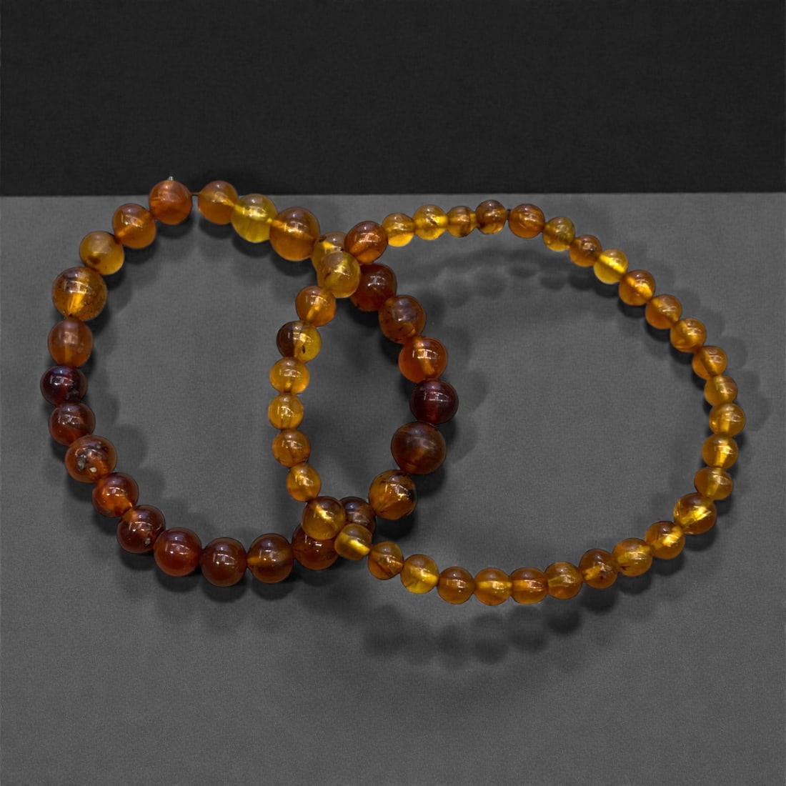 A Group of Two Amber Beaded Bracelets, 13g, 81AA: Comprising two stretch bracelets composed of polished, irregularly spherical amber beads. The amber exhibits a translucent range of warm honey, amber, and reddish-brown hues, with subtle natural inter