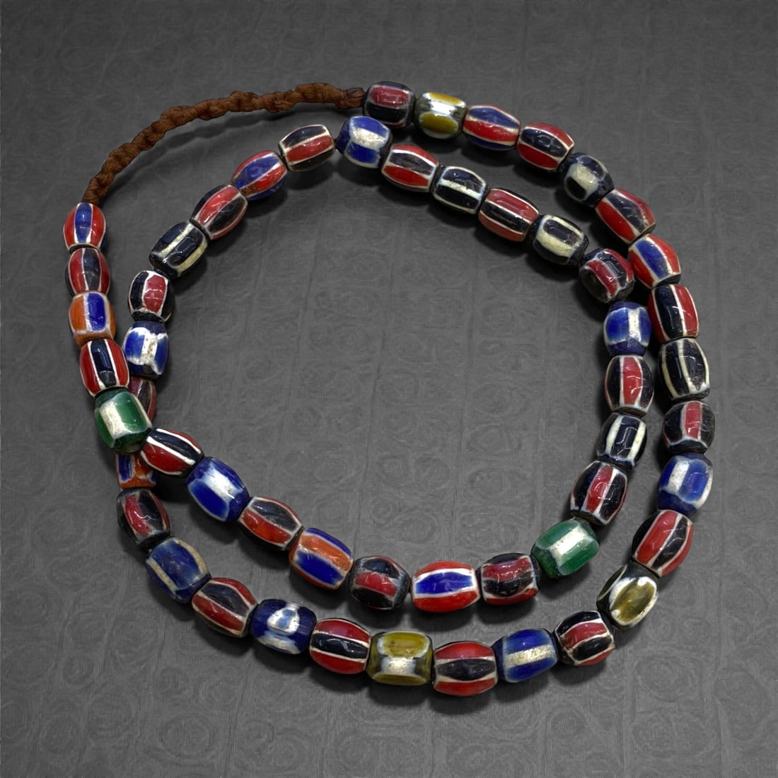 A Venetian Glass Chevron Bead Necklace Strand, 19th Century, 78g, 19AA: Composed of cylindrical glass beads decorated with concentric chevron patterns in red, blue, and white, interspersed with examples featuring green and yellow accents, strung on a modern braided fiber