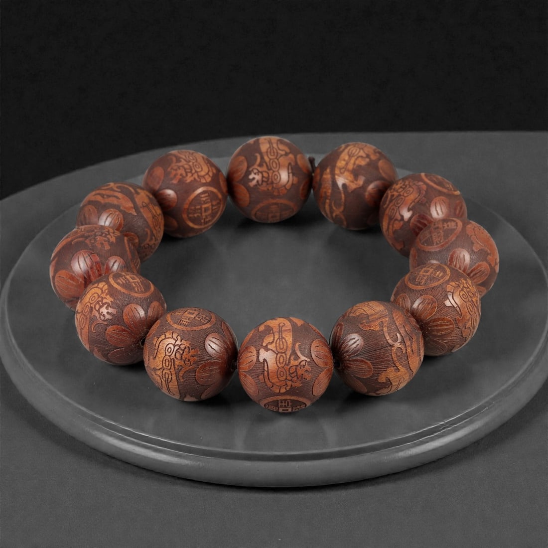 A Chinese Carved Wood Bead Bracelet, 20th Century, 33FD: Composed of spherical beads carved from medium to dark brown wood, each bead worked in relief with stylized decorative motifs. The designs include auspicious symbols, floral elements, and abstracted a