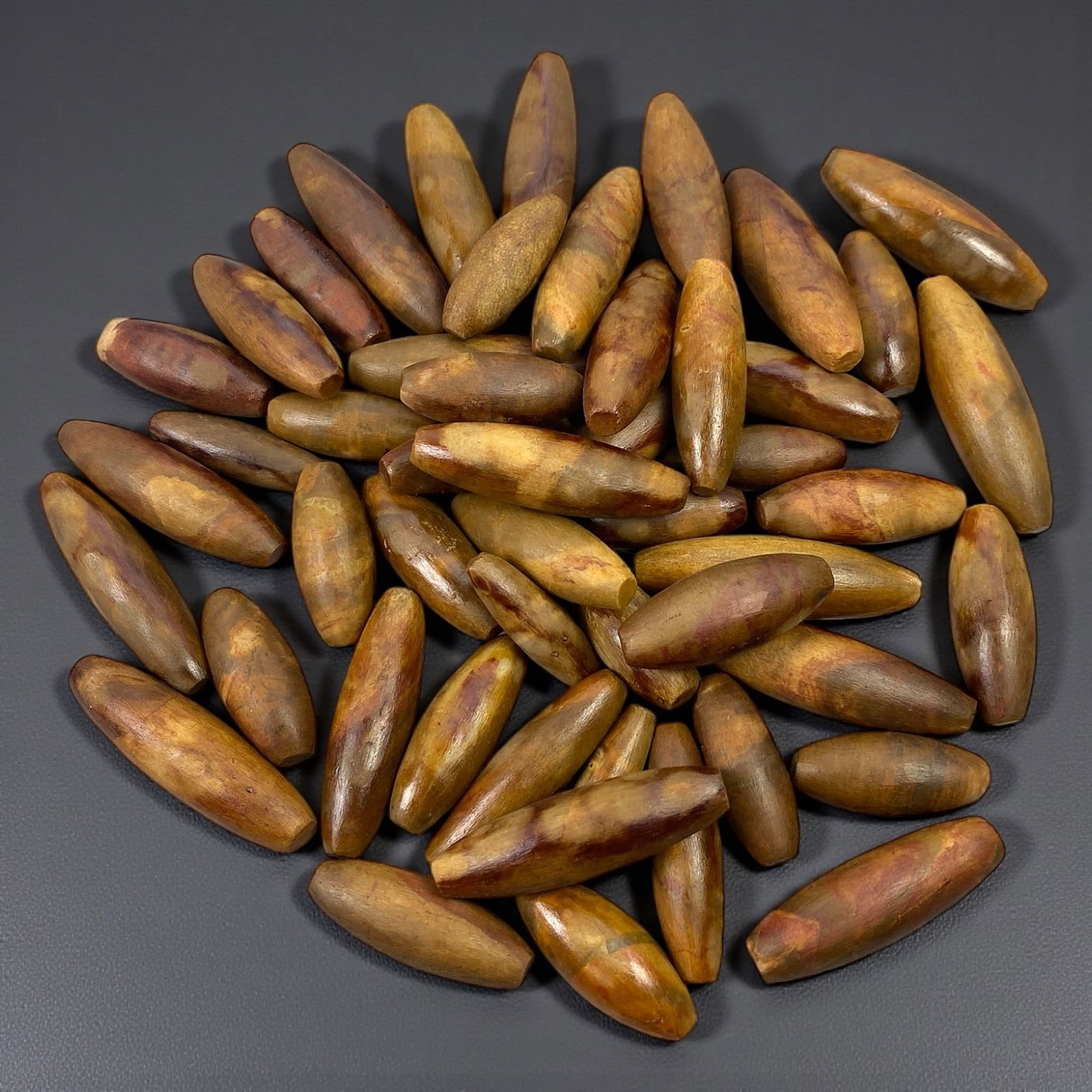 A Group of Himalayan Fossilized Wood Bead Blanks, 20th Century, 82V: Comprising a large group of elongated bead-form elements fashioned from fossilized wood, displaying warm brown, ochre, and russet tones with visible grain patterning and mineralized striations charact