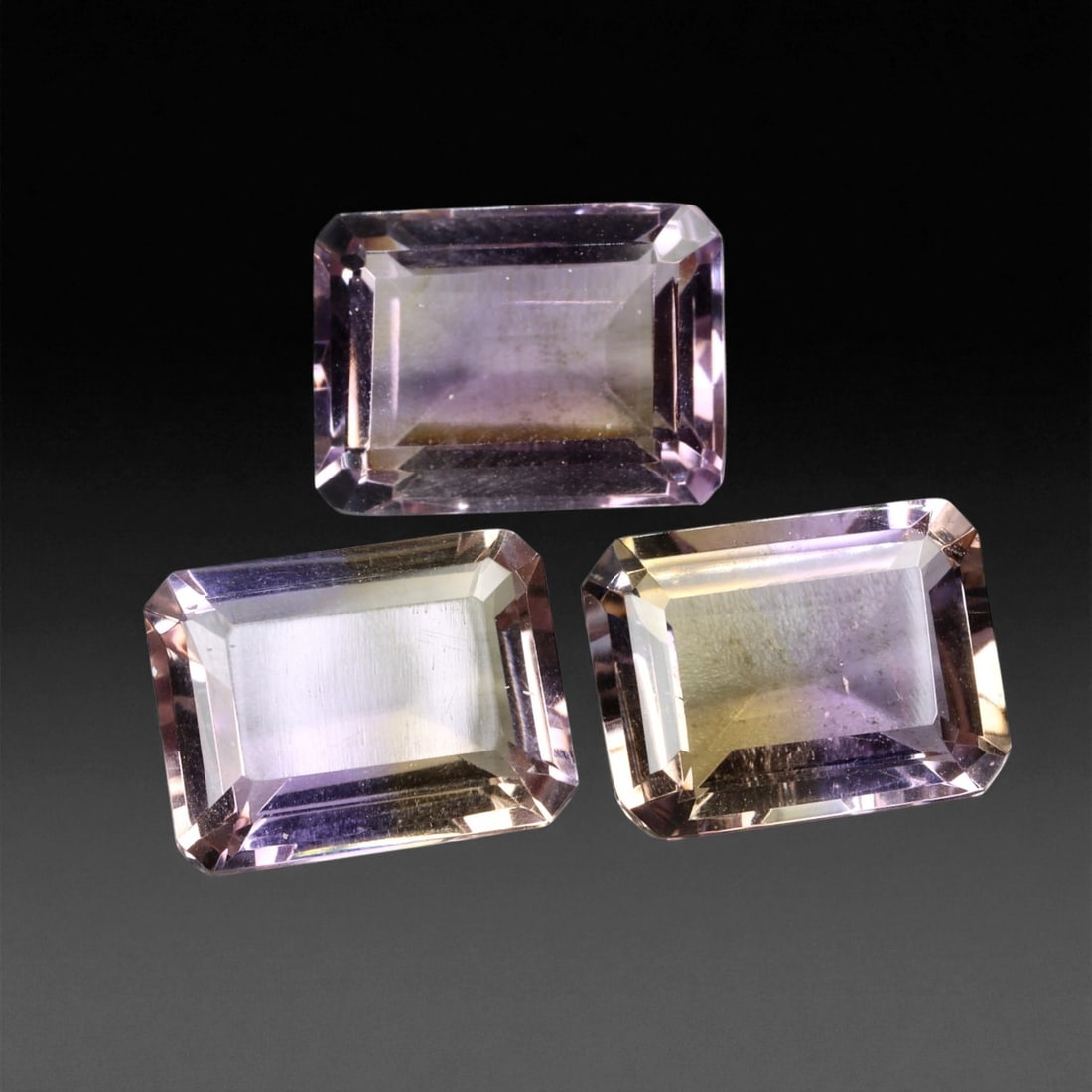 34.54 Carats Light Bi-Color Ametrine Trio - Natural Bolivian Stones - 1.5 to 1.6 cm, 14XE: This trio of emerald-cut ametrines glows with a soft transition of lilac and golden hues, creating an ethereal, pastel palette across each stone. The light saturation and precise faceting deliver a re
