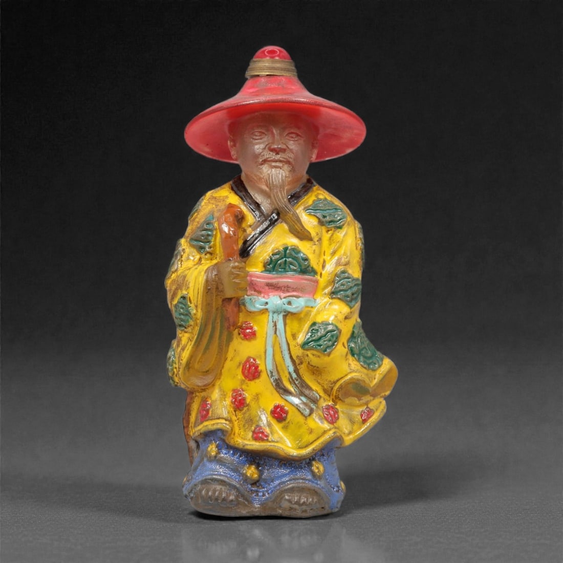 A Chinese Glass Figural Snuff Bottle, 20th Century, 60YC: Molded in translucent and opaque colored glass, the snuff bottle is formed as a standing male figure wearing a wide-brimmed hat and long robe. The figure is rendered in the round, with the hollowed bo
