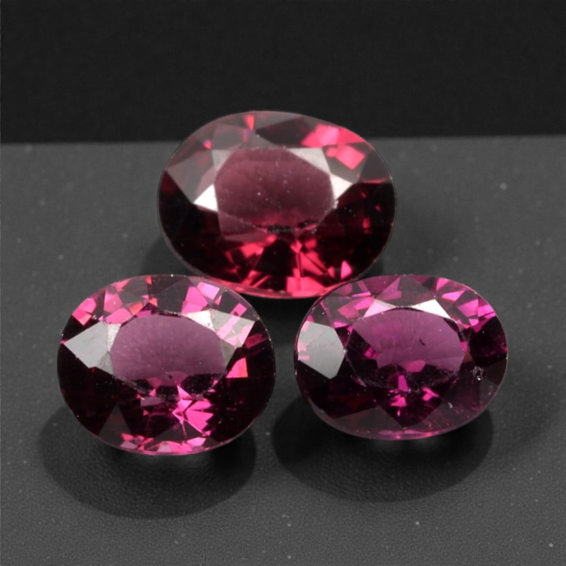 3.14 Carats Deep Raspberry Rhodolite Garnet Selection - Natural Mozambican Stones, 302A: This curated selection of three oval-cut rhodolite garnets captivates with a deep, velvety raspberry hue, reminiscent of ripe summer berries and rich red wine. Each stone is precision-faceted to maxim