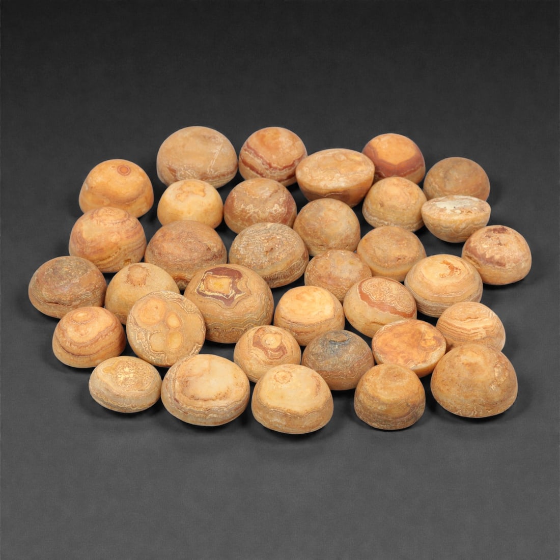 A Group of Tibetan Agate Luk Mik ("Goat's Eye") Beads, 19th-20th Century, 48FK: Comprising thirty-four agate beads carved from banded chalcedony, each bead formed in a hemispherical to lentoid shape with rounded domed upper surfaces and flattened bases, displaying naturally occur