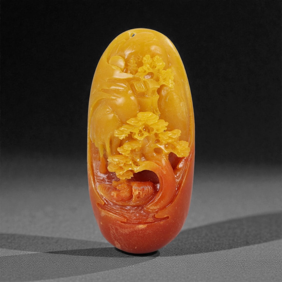 A Chinese Hardstone Landscape Carving, 20th Century, 63YB: Carved from variegated hardstone displaying a natural gradation from warm amber-yellow to deep reddish-brown tones, the plaque is worked in high relief with a compact landscape composition featuring r