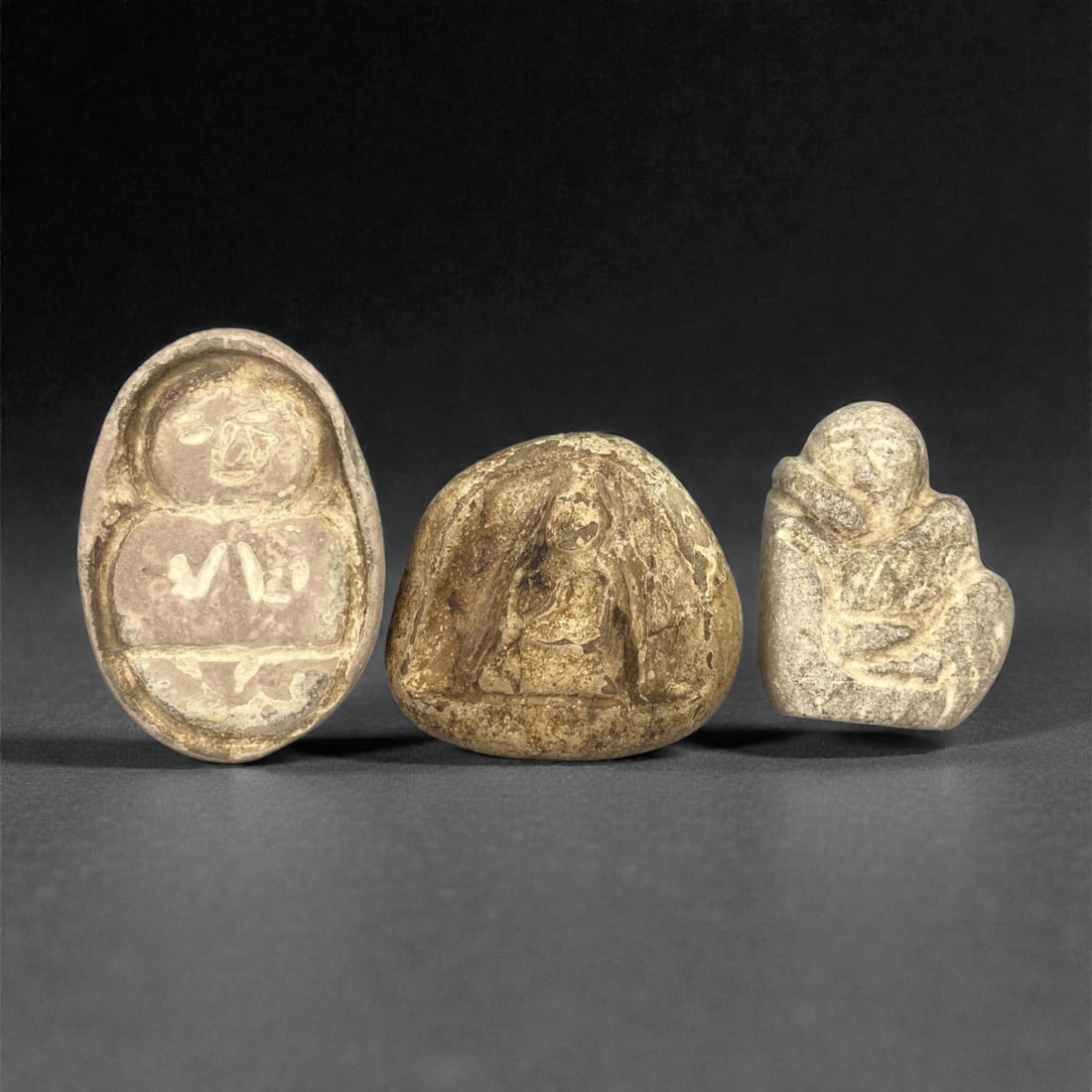 A Group of Three Edo Period Buddhist Stone Carvings, 17th-19th Century, 16FN: Carved from stone with natural tonal variation, surface wear, and mineral encrustation, the three objects depict Buddhist figures in shallow relief, set within irregular stone matrices. The leftmost c