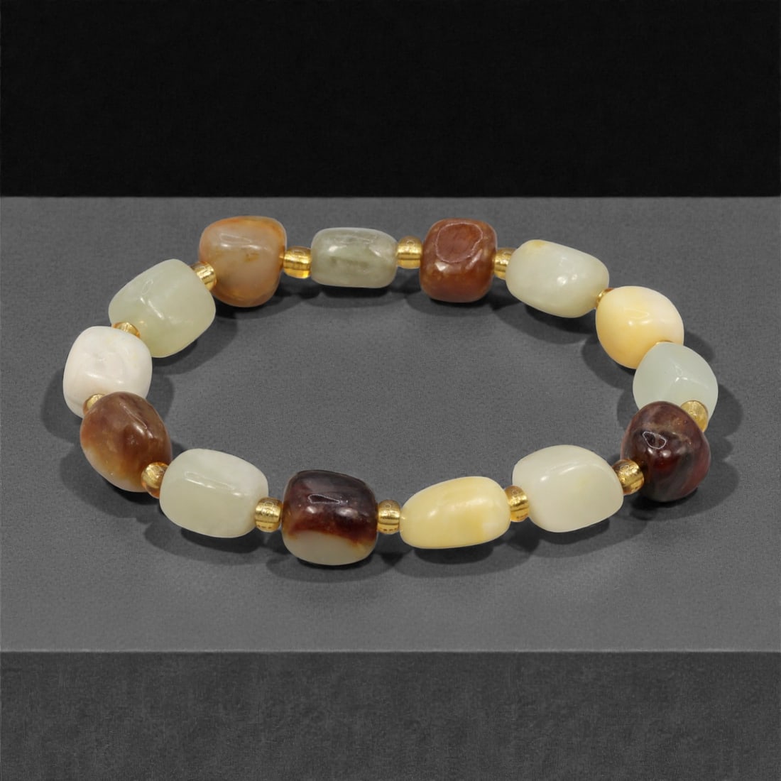 A Chinese Hetian Jade Beaded Bracelet, 20th Century, 54YC: Composed of a continuous strand of rounded rectangular beads carved from Hetian jade, the bracelet displays natural tonal variation ranging from creamy white to pale celadon and russet-brown inclusion