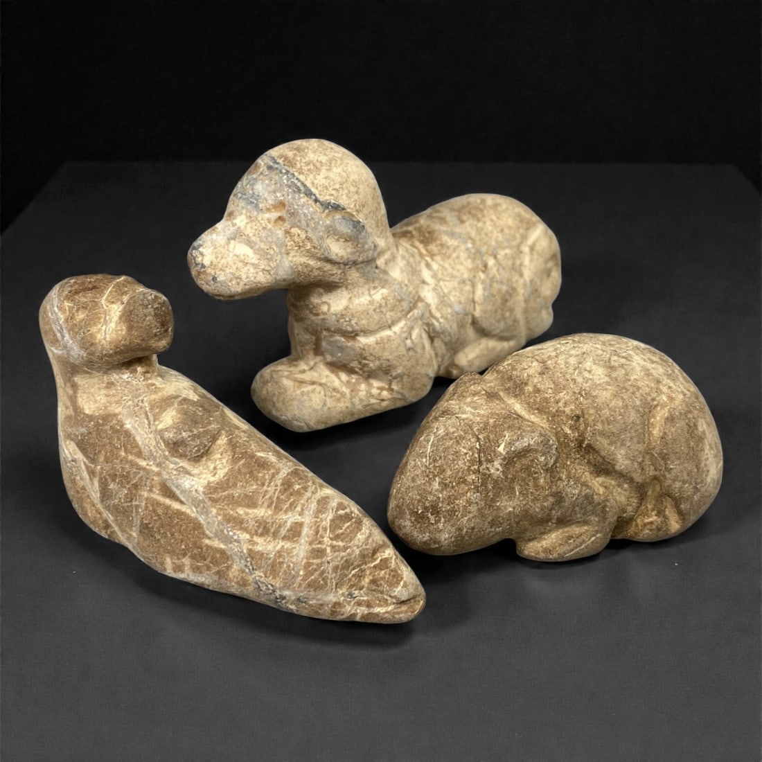 A Group of Three Near Eastern Stone Zoomorphic Effigies, 2nd-1st Millennium BCE, 71FM: Comprising three stone zoomorphic effigies, each formed from light brown stone with visible surface fissures and tonal variation. The leftmost effigy depicts a stylized quadruped in a recumbent pose,