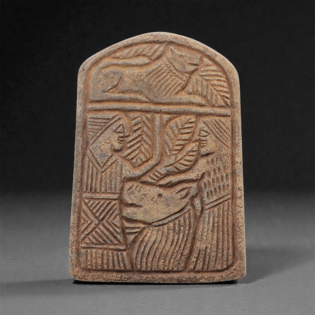 Ancient Near Eastern Lapis Lazuli Relief Plaque, 2nd-1st Millennium BCE, 79FM: An arched-top lapis lazuli relief plaque, measuring 9 x 6.4 cm, with a deep blue matrix and visible calcite inclusions, exhibiting natural surface patina and wear. The plaque is divided into two regis