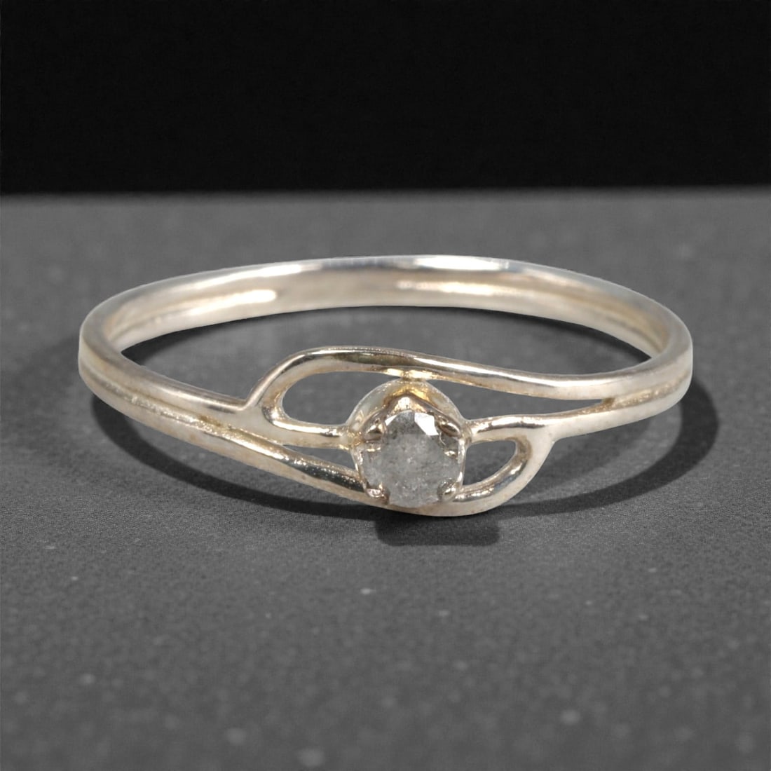 Sterling Silver (925) Ring with Salt-and-Pepper Diamond - Size 7 US, 134A: This modern ring is crafted from polished sterling silver, featuring a distinctive openwork split-shank design that frames the center stone. The centerpiece is a round-cut salt-and-pepper diamond, hel