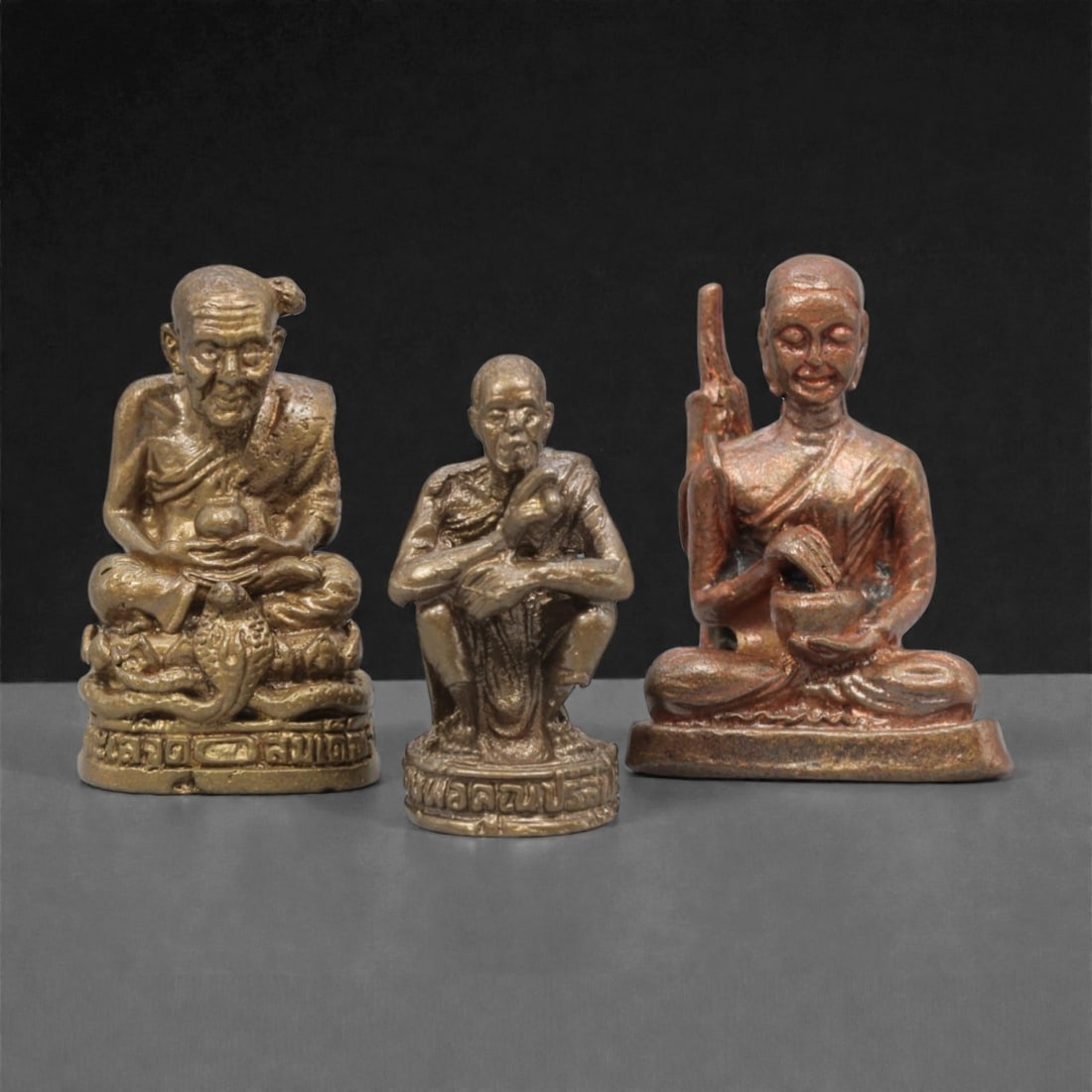 Three Thai Bronze Monk Miniature Figures, 20th Century, 25ZH: Cast from bronze with varied patination, the set comprises three miniature seated monk figures: one with a topknot seated atop a coiled serpent base, one in a crouched pose, and one seated with a staf