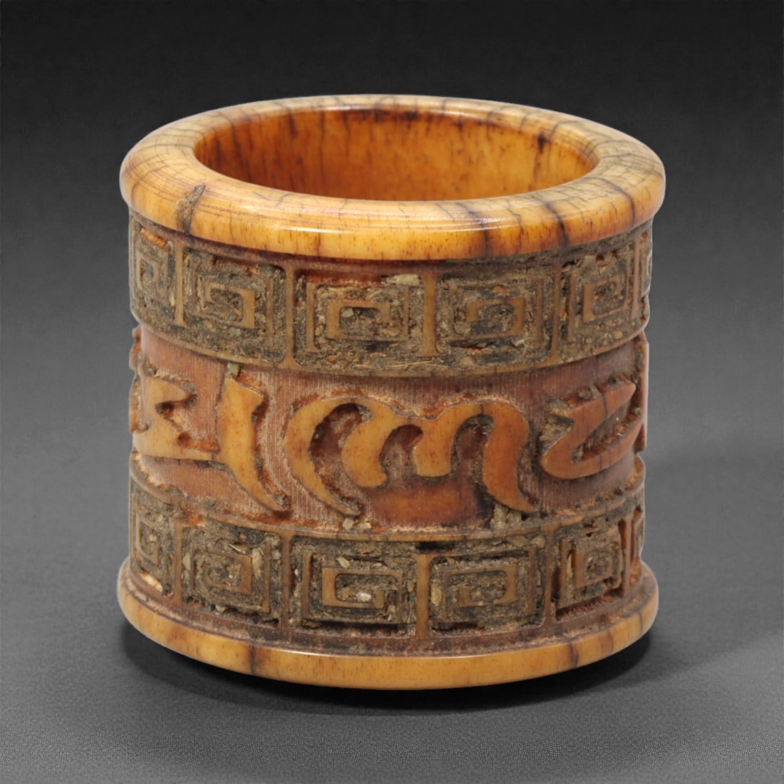 A Tibetan Bone Thumb Ring with Inscription, 20th Century, 88FH: Carved from bone with warm honey-brown coloration and visible natural grain, the thumb ring is cylindrical in form with a thickened wall and hollow interior. The exterior is decorated with carved band