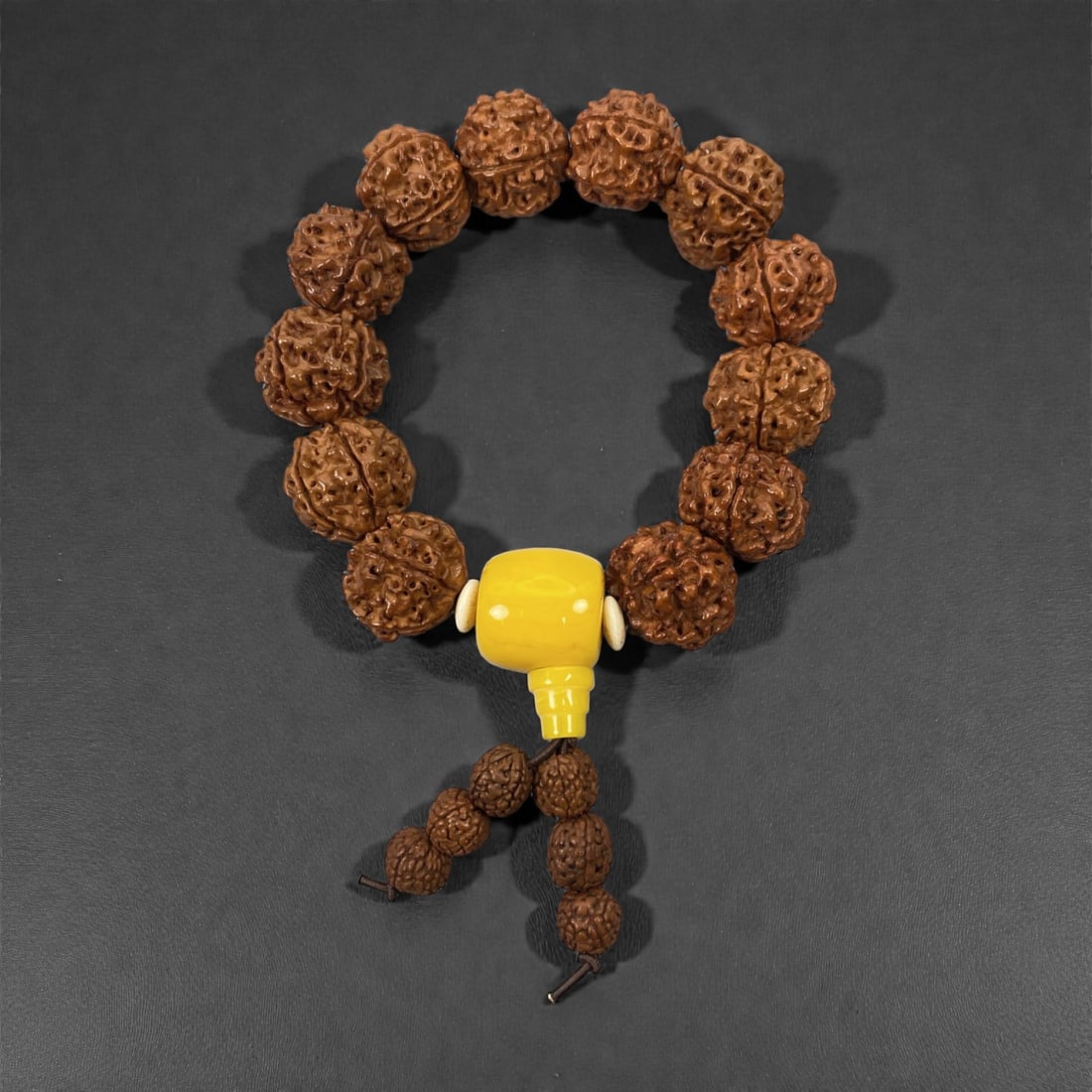 A Chinese Seed Beaded Bracelet with Amber-Resin Finial, 20th Century, 42FJ: The bracelet is composed of a continuous strand of deeply textured natural seed beads, likely rudraksha, each bead displaying a richly carved, multi-lobed surface with a warm brown patina developed th