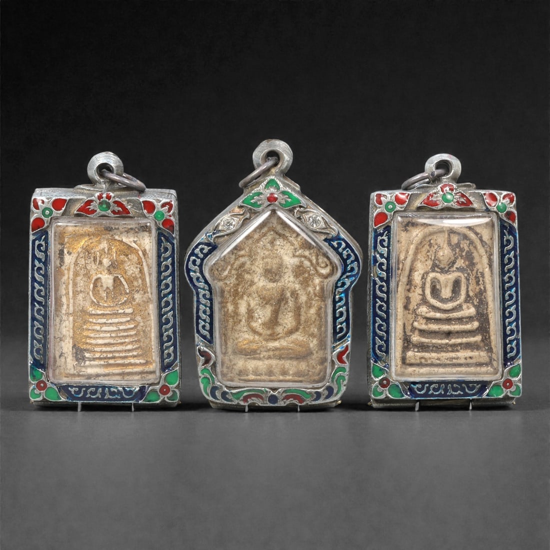 A Group of Thai Clay Buddhist Amulets, 20th Century, 13ZG: Comprising three molded Buddhist amulets formed from pale buff and grey-brown clay compositions, each depicting a seated Buddha in meditation posture upon a stepped base. The figures are rendered in s